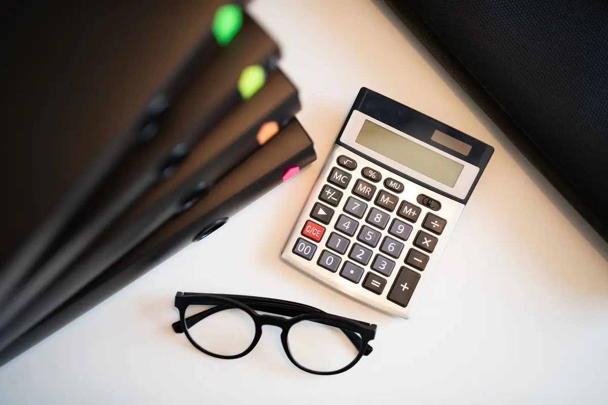 A calculator, reading glasses and client folders on an accounting office desk
