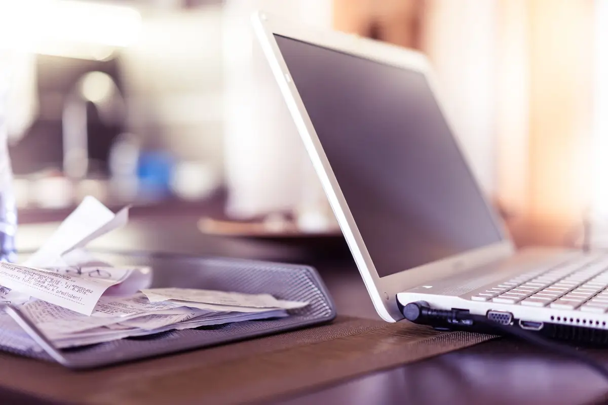 A laptop beside a tray of client receipts waiting to be reconciled