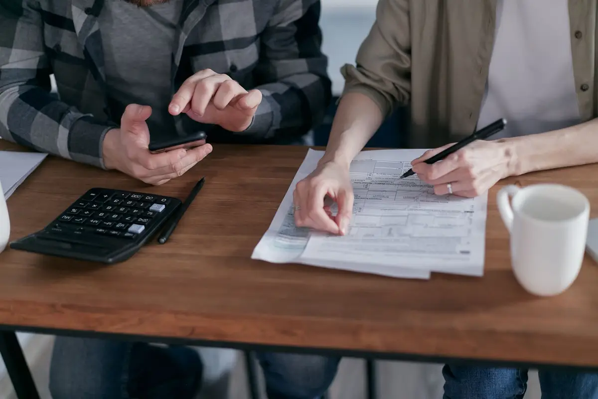 Two people working through tax forms with a calculator at a wooden desk