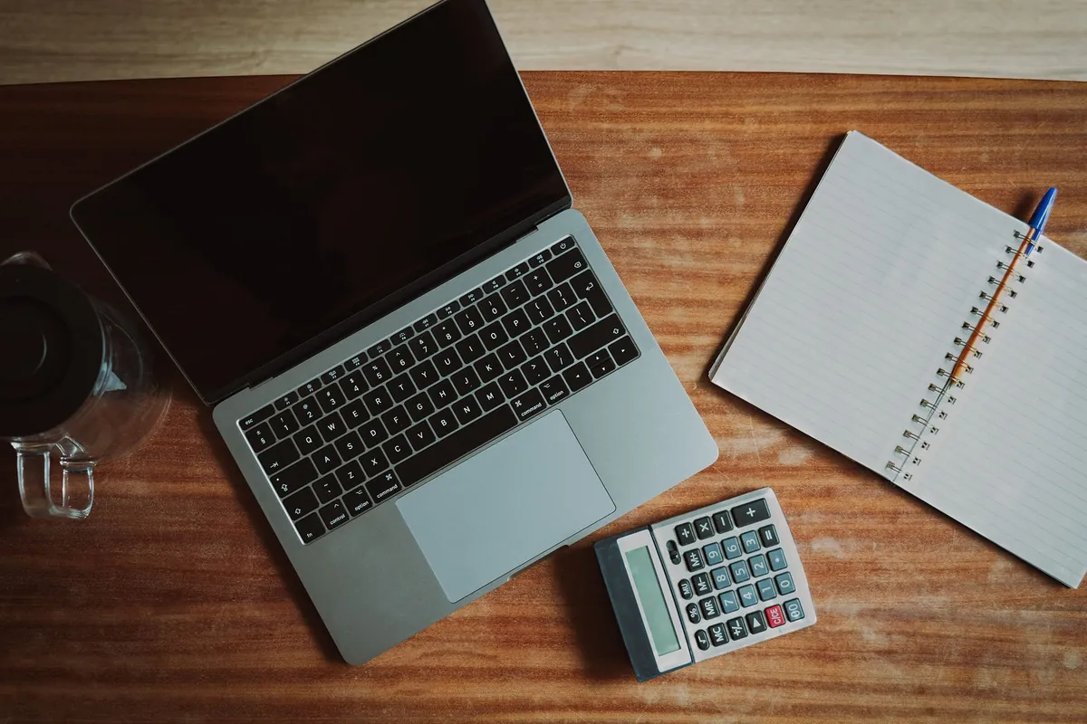 A laptop, an open notebook and a calculator on a wooden desk